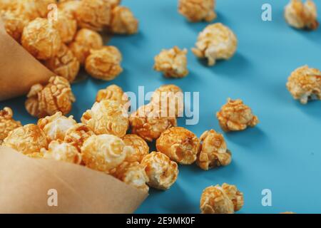 Karamell Popcorn in einem Papierumschlag auf blauem Hintergrund. Köstliches Lob für das Ansehen von Filmen, Serien, Cartoon. Freier Speicherplatz, Nahaufnahme. Minimalis Stockfoto