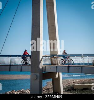 Fuengirola, Malaga, Spanien. Januar 2021. Zwei Personen, die an einem sonnigen Wintermorgen auf einer Hängebrücke in Fuengirola Fahrrad fahren. Stockfoto