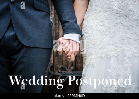 Hochzeit verschoben wegen Covid 19 Pandemie Sperrbeschränkungen rot Text schreiben und Nahaufnahme der Braut in Kleid Den Bräutigam in der Hand halten Stockfoto