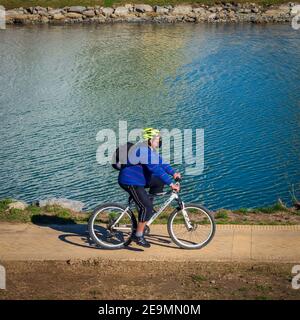 Ein älterer Mann, der an einem sonnigen Wintermorgen mit einer Maske im Flusspark Fuengirola Fahrrad fährt. Stockfoto