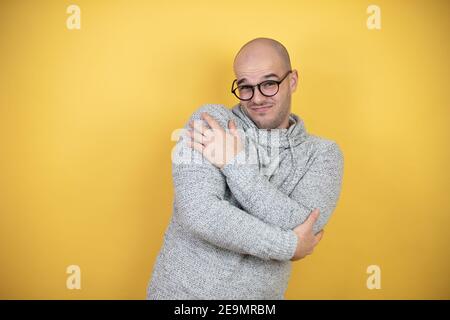 Junge Glatze Mann trägt Brille über gelben Hintergrund umarmt sich glücklich und positiv, lächelnd zuversichtlich Stockfoto