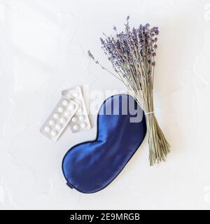 Flache Lay Komposition mit Lavendelblüten, Maske für Schlaf und Schlaftabletten auf einem weißen Hintergrund. Behandlung von Schlaflosigkeit oder Depressionen Stockfoto