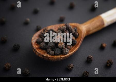 Organische ganze schwarze Pfefferkörner in einem Holzlöffel. Low-Taste. Nahaufnahme. Stockfoto