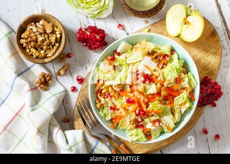 Diätsalat frisches Gemüse aus Chinakohl, Karotten, Apfel, Nüssen und Granatapfel mit Vinaigrette-Dressing auf einem weißen Holztisch. Draufsicht FLA Stockfoto