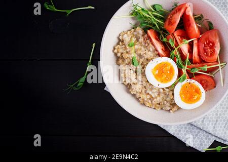 Frühstück Haferbrei Haferbrei mit gekochtem Ei, Kirschtomaten und Microgreens. Gesunde, ausgewogene Ernährung. Draufsicht, oben, Kopierbereich Stockfoto