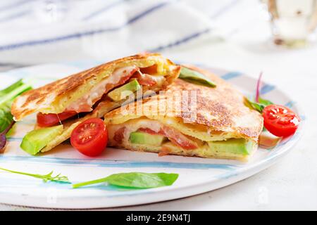 Leckeres Frühstück mit Quesadilla und Eiern. Mexikanische Küche. Trendgerichte mit Omelette, Käse, Tomaten, Avocado. Einfaches und leichtes Mittagessen. Stockfoto