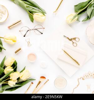 Weiblicher Arbeitsplatz mit gelben Tulpenblüten, Damenmode goldene Accessoires, Tagebuch, Gläser auf weißem Hintergrund. Flach liegend. Draufsicht Hintergrund. Stockfoto