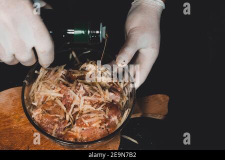 Der Mann Schnitt einen Schweinehals, marinierte ihn in Gewürze, gab ihn in eine Schüssel und fügte Olivenöl hinzu, das Fleisch wurde für barbecue,2020 mariniert Stockfoto