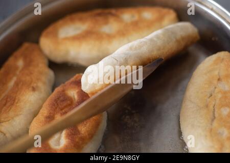 In einer Pfanne mit Pflanzenöl werden Torten mit Füllung gebraten, die mit einem Holzspatel umgedreht werden Stockfoto