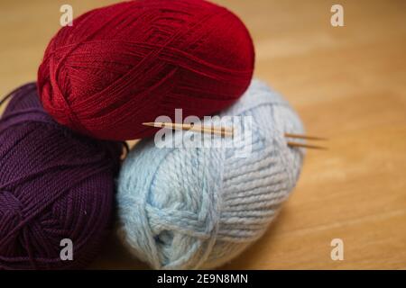 Ein lockerer Stapel von Knäueln in verschiedenen Farben des Strickgarns mit zwei kleinen Nadeln hervorstehend. Künstlerische Schärfentiefe Hintergrund von Holztisch. Stockfoto