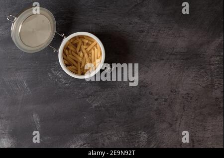 Detail eines weißen Keramikglases mit Deckel mit Makkaroni Innen auf dunklem Hintergrund Stockfoto