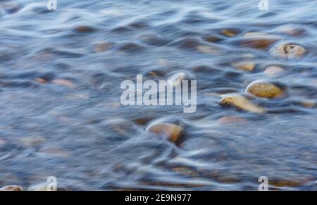 Nahaufnahme von bewegungsunscharfen Wasserriffeln, die über einem Cobble Stone fließen Flussbett Stockfoto