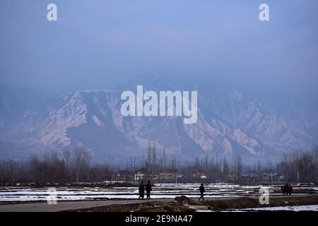 Pendler gehen entlang der Straße mit schneebedeckten Bergen im Hintergrund während eines Winterabends in Srinagar.Wetter über die Stadt Srinagar hat sich verbessert, nachdem Kaschmir frischen Schneefall erhielt. Die Mindesttemperatur blieb über dem Gefrierpunkt in der Stadt Srinagar, da das Wetterbüro das trockene Wetter für die nächsten sieben Tage prognostizierte. Stockfoto