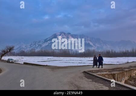 Pendler gehen entlang der Straße mit schneebedeckten Bergen im Hintergrund während eines Winterabends in Srinagar.Wetter über die Stadt Srinagar hat sich verbessert, nachdem Kaschmir frischen Schneefall erhielt. Die Mindesttemperatur blieb über dem Gefrierpunkt in der Stadt Srinagar, da das Wetterbüro das trockene Wetter für die nächsten sieben Tage prognostizierte. Stockfoto