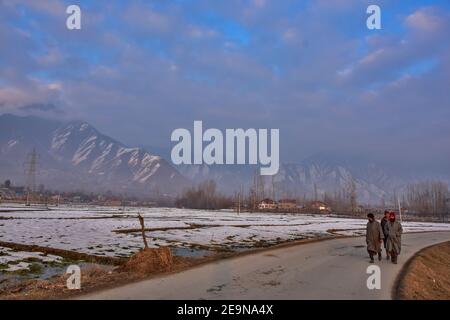 Pendler gehen entlang der Straße mit schneebedeckten Bergen im Hintergrund während eines Winterabends in Srinagar.Wetter über die Stadt Srinagar hat sich verbessert, nachdem Kaschmir frischen Schneefall erhielt. Die Mindesttemperatur blieb über dem Gefrierpunkt in der Stadt Srinagar, da das Wetterbüro das trockene Wetter für die nächsten sieben Tage prognostizierte. Stockfoto