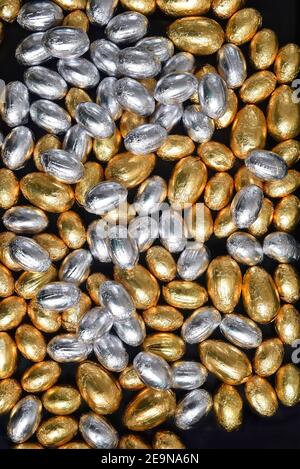 Große & kleine gelbe, Gold und Silber Folie umwickelt Schokolade ostereier, vor einem schwarzen Hintergrund. Stockfoto