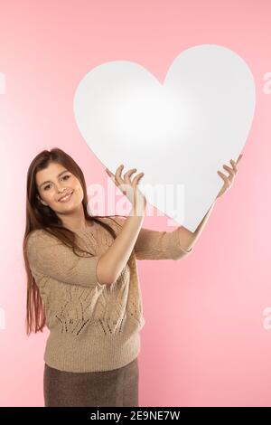 Ein schönes Mädchen in der Liebe hält eine Herzform in ihrer Hand. Junge Frau will eine schöne Herzform als Symbol der Liebe am Valentinstag zu geben. Stockfoto