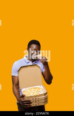 Lustige schwarze Kurier isst Stück Pizza und hält 4 Pizzaboxen. 2+2 großer Rabatt für Kunden. Leckeres Essen Pizzalieferung vom Restaurant. Sicherheitsabsch Stockfoto