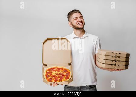 Lustige junge kaukasischen Kurier mit Pizza und 4 Karton mit Pizzen. Ein hübscher Mann hält Pizza und lächelt. Werben Sie für Pizzeria Lieferung bei coro Stockfoto