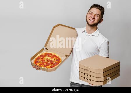 Lustige junge kaukasischen Kurier mit Pizza und 4 Karton mit Pizzen. Ein hübscher Mann hält Pizza und lächelt. Werben Sie für Pizzeria Lieferung bei coro Stockfoto