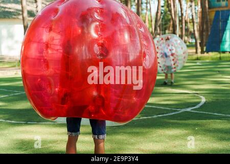 Bubble Fußball Sport Spiel. Fußballspieler spielen Bumperball auf dem grünen Feld. Teambildung. Mann in Blase Ballon laufen. Stockfoto