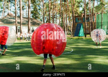 Bubble Fußball Sport Spiel. Fußballspieler spielen Bumperball auf dem grünen Feld. Teambildung. Mann in Blase Ballon laufen. Stockfoto