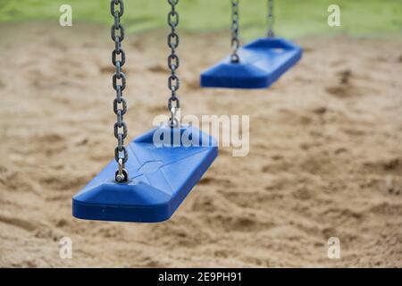 Zwei leere blaue Plastikschaukeln für Kinder hängen an Metallketten auf einem Spielplatz während des Lockdown in der Coronavirus-Pandemie, Kopierraum, selecte Stockfoto