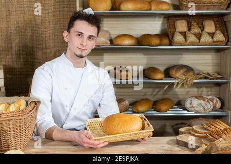 Ein Angestellter sitzt hinter der Theke und serviert seine eigenen Backwaren. Ein gutaussehender Bäcker bedient seine Kunden in einer Bäckerei der Familie. Stockfoto