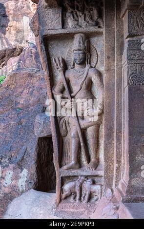 Badami, Karnataka, Indien - 7. November 2013: Höhlentempel über dem Agasthya See. Nahaufnahme von grimmiger grauer Steinzwerapalaka mit Dreizack-Skulptur bei Entr Stockfoto