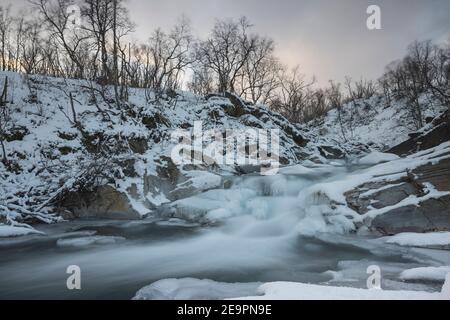 Eisiger Wasserfall im Schnee in Long expo Stockfoto