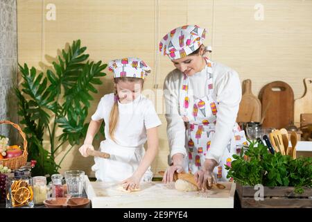 Die Mädchen, also Mutter und fünfjährige Tochter, Rollen Pizzateig mit einem speziellen Holzpfropfen auf dem Brett aus, das auf der Küchentheke platziert ist. Stockfoto