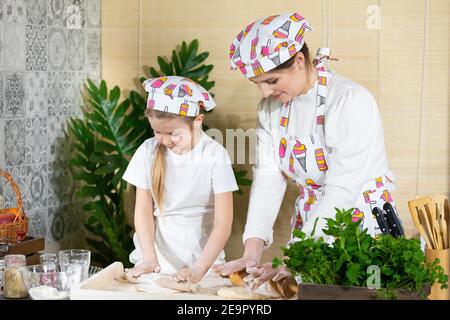 Die Mädchen, also Mutter und fünfjährige Tochter, Rollen Pizzateig mit einem speziellen Holzpfropfen auf dem Brett aus, das auf der Küchentheke platziert ist. Stockfoto