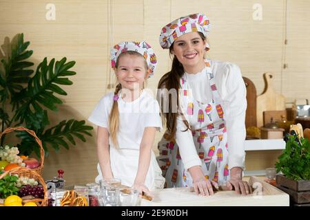 Die Mädchen, also Mutter und fünfjährige Tochter, Rollen Pizzateig mit einem speziellen Holzpfropfen auf dem Brett aus, das auf der Küchentheke platziert ist. Stockfoto