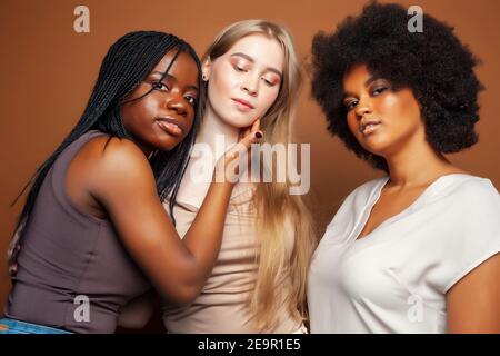 Junge hübsche kaukasische, afro, skandinavische Frau posiert fröhlich zusammen auf braunem Hintergrund, Lifestyle diverse Nationalität Menschen Konzept Stockfoto