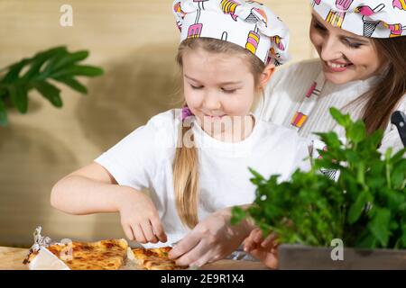 Nach dem Backen der hausgemachten Pizza begannen Tochter und Mutter zu dekorieren und frische Kräuter auf die Pizza zu geben. Die Freude der gemeinsamen Momente von Mutter und Tochter während der Arbeit in der Küche. Stockfoto