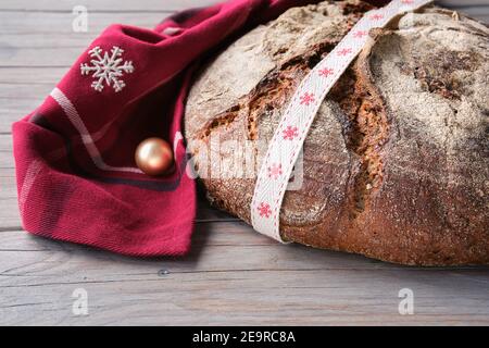Weihnachtsbacken. Vollkornbrot Roggen Weizenbrot Ofen in Keramikpfanne gebacken. Kein handgefertigtes Brot auf Schneidebrett auf Holz mit festlichem dunkelrotem Handtuch XM kneten Stockfoto