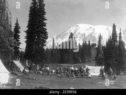 Bergsteiger und Camper im Zeltlager am Paradise Park mit Kletterausrüstung, zeigt Mount Rainier im Hintergrund, ca. Stockfoto