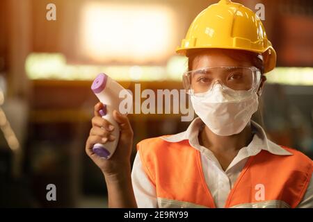 Industriearbeiterinnen tragen Gesichtsmaske und überprüfen die Körpertemperatur während der Coronavirus (COVID-19) Pandemie. Stockfoto