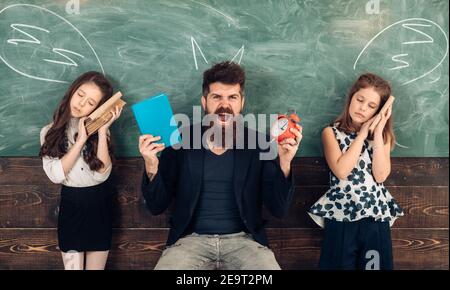 Die Schüler sind müde vom Studium in der Schule. Der Lehrer schreit schläfrige Schüler an. Tutor mit Wecker und Buch. Zeit, um Konzept zu lernen. Stockfoto