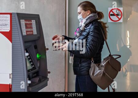 Eine Frau, die eine medizinische Schutzmaske auf ihrem Gesicht trägt Einsetzen einer Kreditkarte und Abheben von Bargeld von einem GELDAUTOMAT Stockfoto