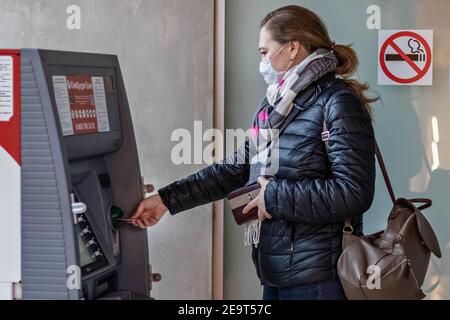 Eine Frau, die eine medizinische Schutzmaske auf ihrem Gesicht trägt Einsetzen einer Kreditkarte und Abheben von Bargeld von einem GELDAUTOMAT Stockfoto