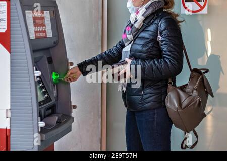 Eine Frau, die eine medizinische Schutzmaske auf ihrem Gesicht trägt Einsetzen einer Kreditkarte und Abheben von Bargeld von einem GELDAUTOMAT Stockfoto