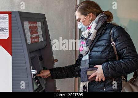 Eine Frau, die eine medizinische Schutzmaske auf ihrem Gesicht trägt Einsetzen einer Kreditkarte und Abheben von Bargeld von einem GELDAUTOMAT Stockfoto