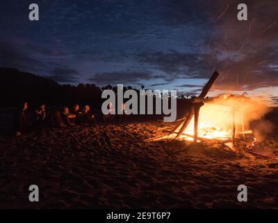 Wanderer drängen sich am Ende des heaphy Trail an der Westküste Neuseelands um ein Lagerfeuer am Strand. Stockfoto