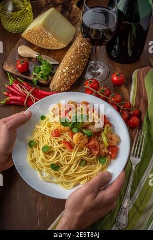 Spaghetti mit Garnelen, Kirschtomaten und Gewürzen auf Holzhintergrund. Hintergrund für das Essen. Stockfoto