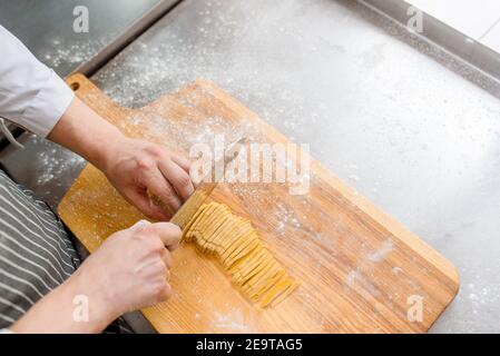 Der Koch schneidet mit einem Messer rohe Nudeln mit Mehl. Schneiden Nudeln in der Küche . Der Koch kocht Spaghetti im Restaurant. Stockfoto