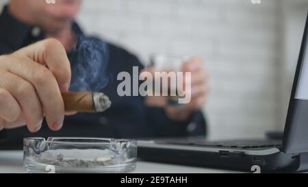 Geschäftsmann verschwommenes Bild trinken Whisky Rauchen Zigarre und Arbeiten am Laptop Stockfoto