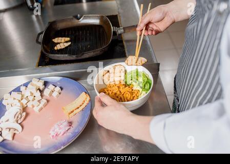 Gebratenes Hähnchenfilet wird auf den Teller gelegt. Der Koch kocht Spaghetti-Nudeln für Ramen-Suppe. Kochen Ramen Suppe mit Fleisch, Pilze, Rettich, Eier. Stockfoto