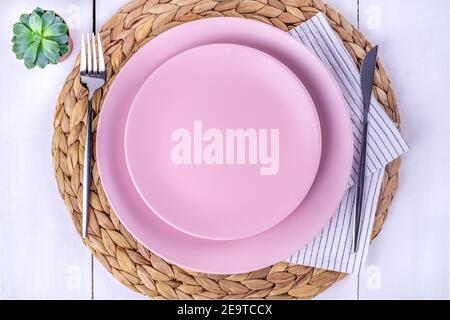 Nahaufnahme von oben eine Portion von zwei leeren rosafarbenen Tellern, einem Messer und einer Gabel auf einem Strohhalm umweltfreundliche Serviette. Selektiver Fokus. Mockup, Minimalismus. Stockfoto