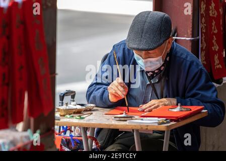 Hongkong, Hongkong, China. Februar 2021, 6th. Eine Kalligraphie sifu (Meister) arbeitet an der Seite einer belebten Straße in Causeway Bay Hongkong und produziert handbemalte kantonesische Couplets, die für das chinesische Neujahr bereit sind. Mondneujahrescouplets oder Cheun lyun, werden als Dekoration verwendet und haben unterschiedliche glückverheißende Nachrichten, die auf ihnen geschrieben werden. CNY wird am Freitag, 12th. Februar 2021 mit dem Feiertag beginnen, der das Tierkreisjahr des Ochsen ankündigt. Quelle: Jayne Russell/ZUMA Wire/Alamy Live News Stockfoto